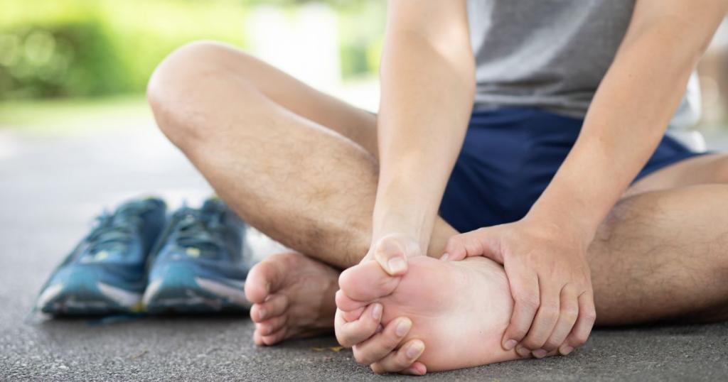 person sitting down outside holding their painful top foot with tennis shoes beside them