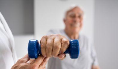 Elderly man lifting dumbel practicing hand therapy with assistance from a physical therapist